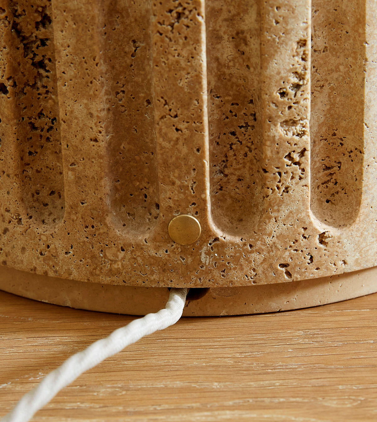 Close-up of a textured brown lamp base with a visible power cord on a wooden surface.