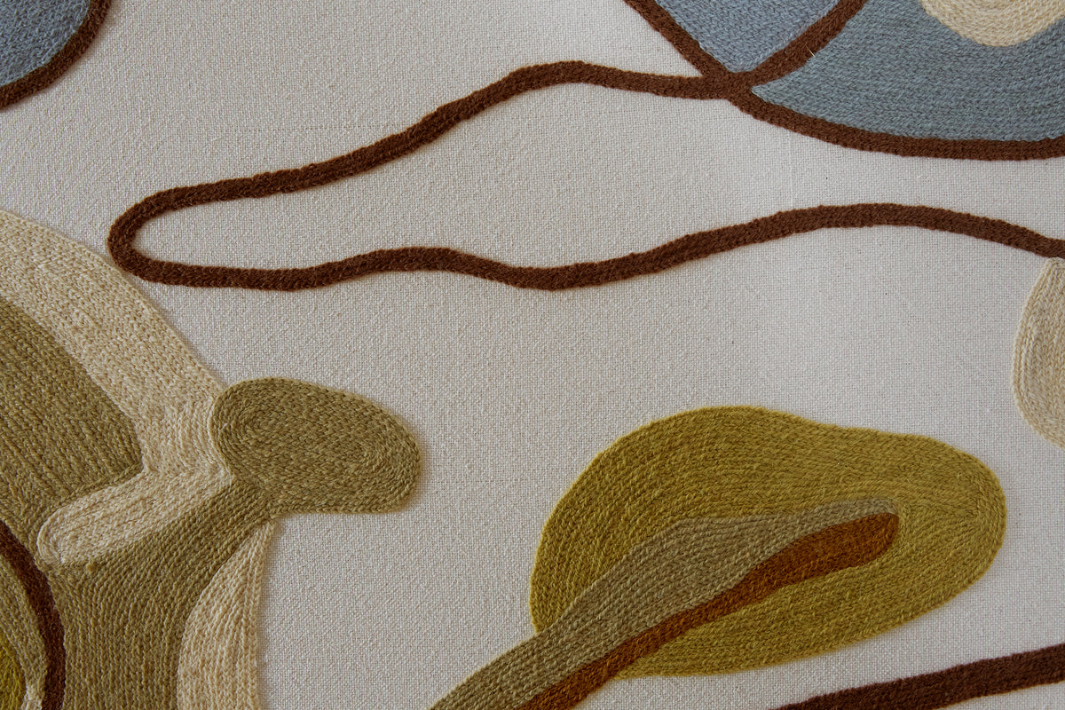 Close-up of a crewel work headboard with abstract patterns in brown, beige, blue and green.